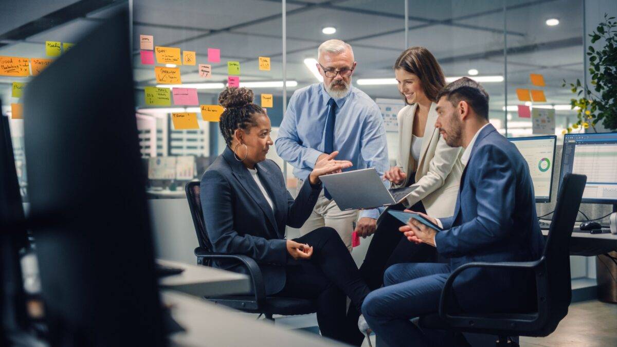 Team of professionals talking in an office and looking at a laptop